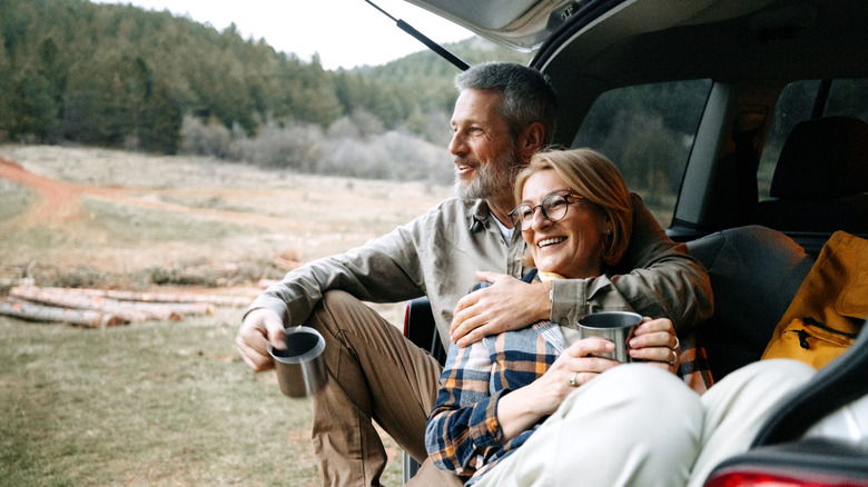 A retirement-age couple smiling and sitting in the back of car with trunk open