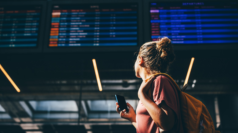 traveler looking up at airport flight schedule screen