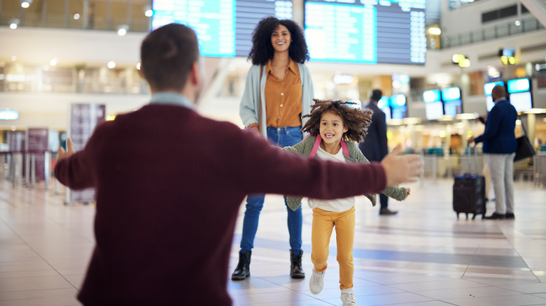 A smiling child running toward an adult in a bright airport terminal