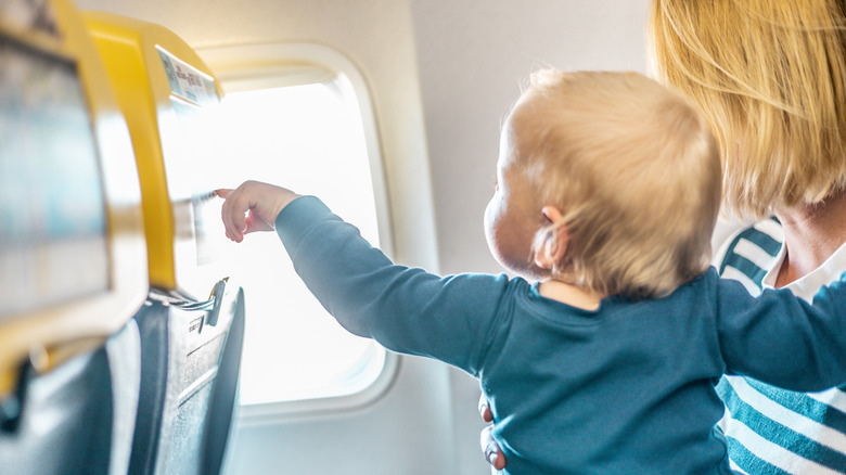 Mother holding a baby on an airplane, while the child points at the touch screen.
