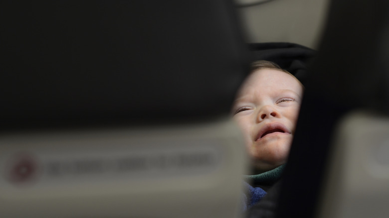A sad baby cries on an airplane.