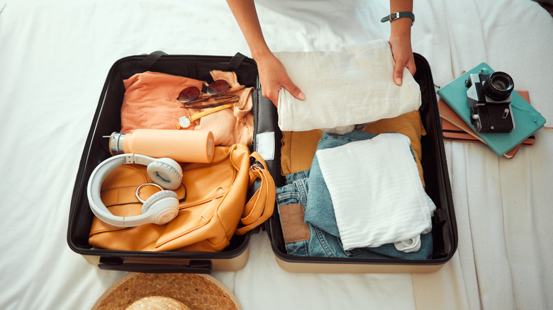 person folding clothes and packing open suitcase