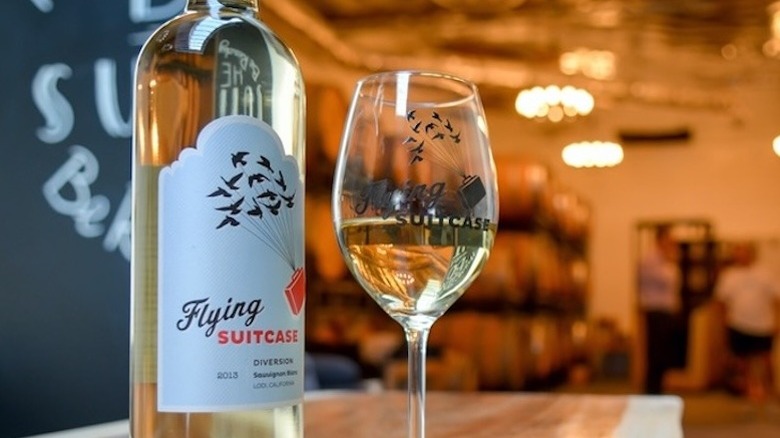 A bottle of Flying Suitcase wine with a glass of white wine
