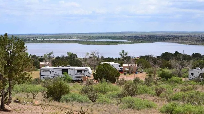 White RVs and trailer camp between pines around a large lake in New Mexico.