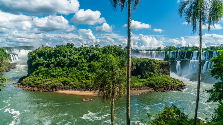 The Iguazú Falls to the right of the islet in the Argentinian Iguazú National Park, with people touring on a boat