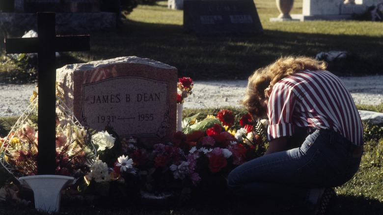 A woman kneels at James Dean's grave surrounded by flowers in Fairmount, Indiana