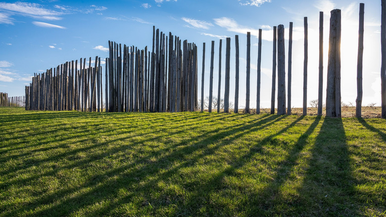A stockade of vertical logs casting shadows on a green prarie