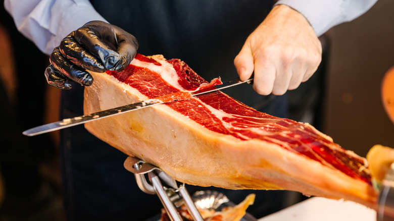 A person slicing a piece of jamon from Spain
