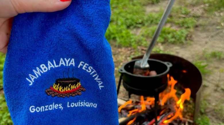 Person holding Jambalaya Festival towel near outdoor firepit