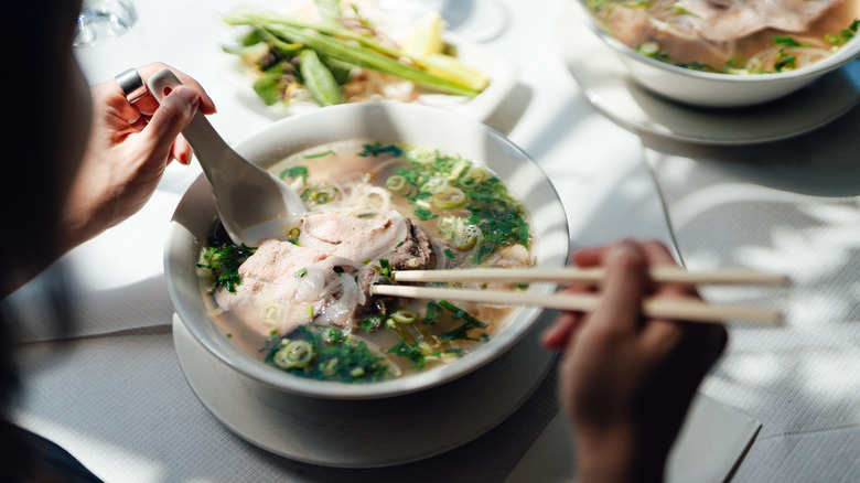A woman eating pho in a white bowl