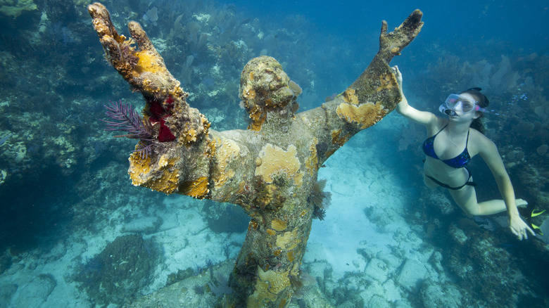 An underwater statue of Christ with arms outstretched and a snorkeler