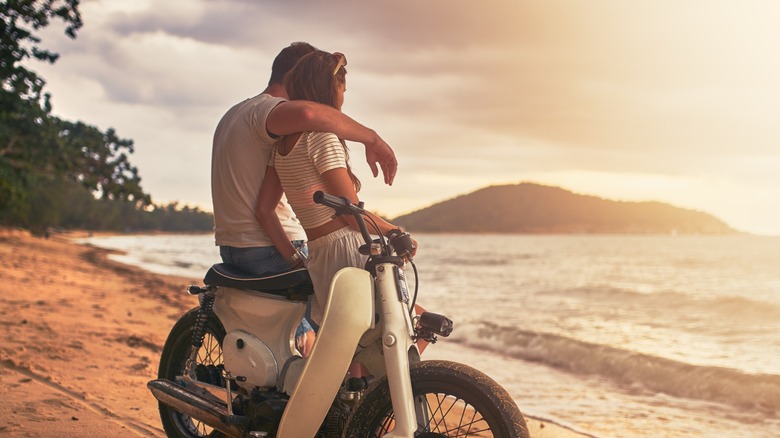 Couple watches the sunset from a vintage bike on the beach in Koh Samui, Thailand