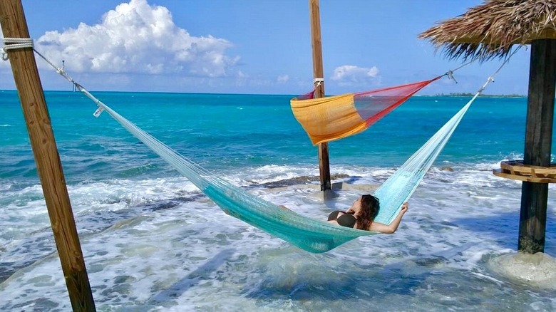 A person casually relaxing in a hammock overlooking the turquoise water on Rose Island in The Bahamas