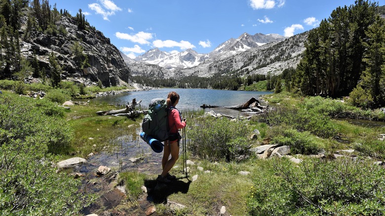 A backpackaer enjoys a view of snowy mountains beside a lake