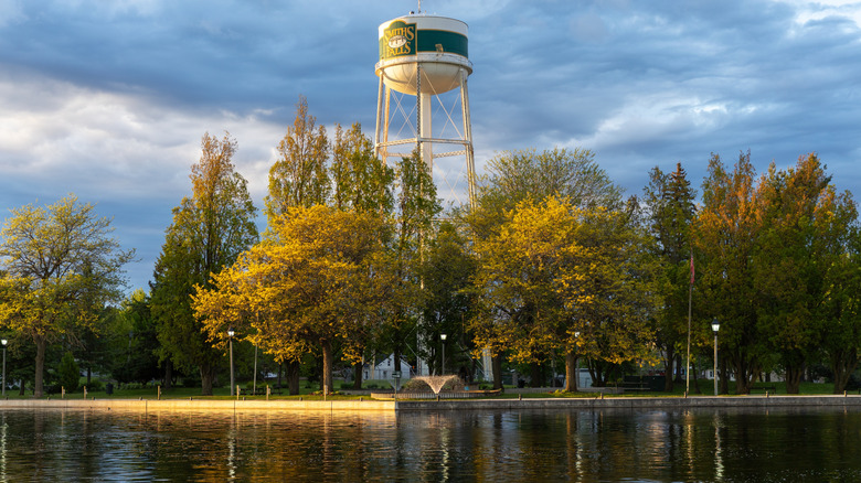 Water tower with green and gold colors soaring above riverfront against bruised sky