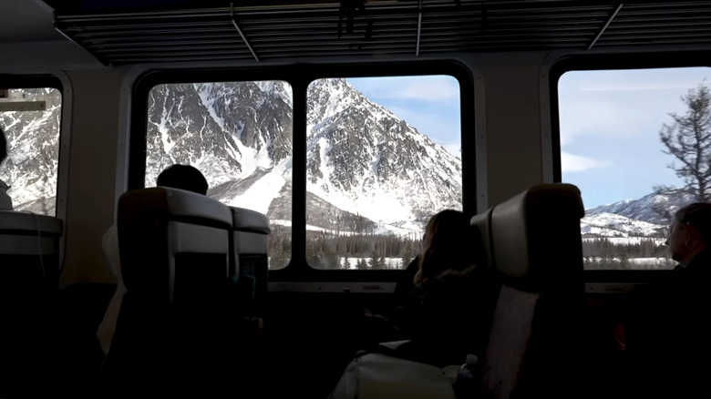 passengers looking at snowy mountains through large windows from inside the Aurora Winter Train