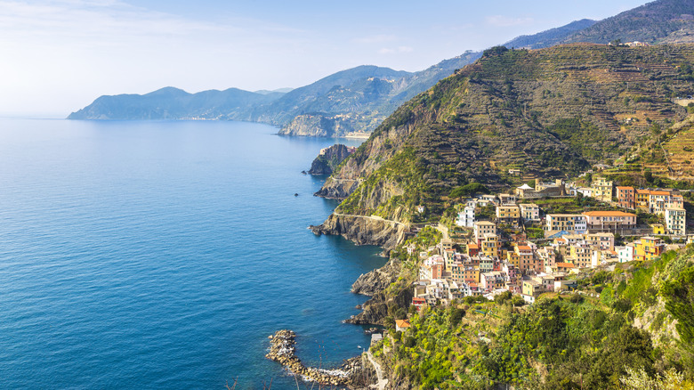 View of Cinque Terre's buildings on a cliff, above turquoise waters, and surrounded by hills