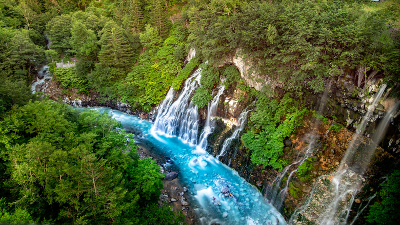 Shirahige Waterfall ice blue water with green trees in Hokkaido, Japan