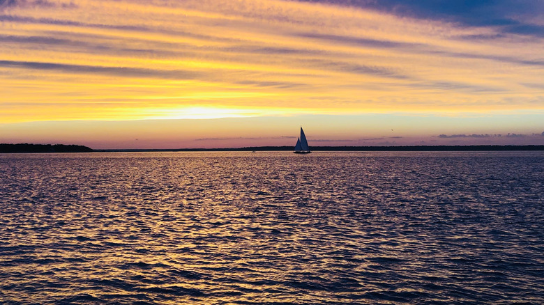 an ocean with a sail boat on it beneath a yellow sunset