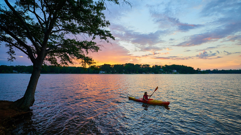 A woman kayaking on a calm lake during sunset
