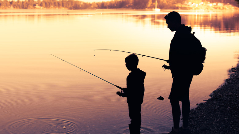 Silhouette of a father and son fishing on the water's edge at dusk