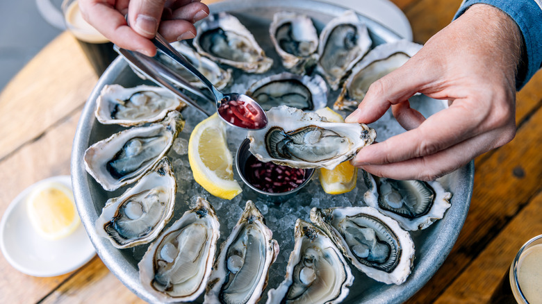 Hands holding a fresh oyster over an icy platter