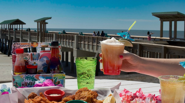 Hand holding frozen drink with Folly Beach Pier in the backdrop