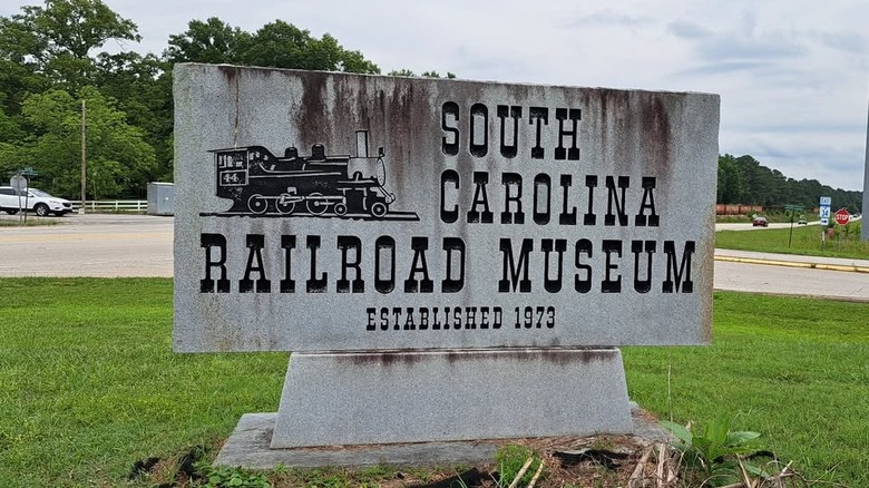 stone sign with black text on green grass under overcast sky