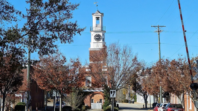 blue sky over white and red brick clock tower over road with power lines and brown leaves on trees