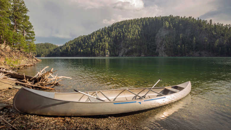 Canoe pulled up on shore of lake, with trees behind