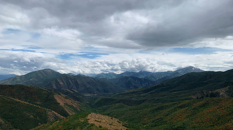 Uinta-Wasatch-Cache National Forest, Utah, USA - September 13, 2022: Expansive mountain range with rolling green hills under a vast, cloud-filled sky, creating a serene and majestic landscape view.