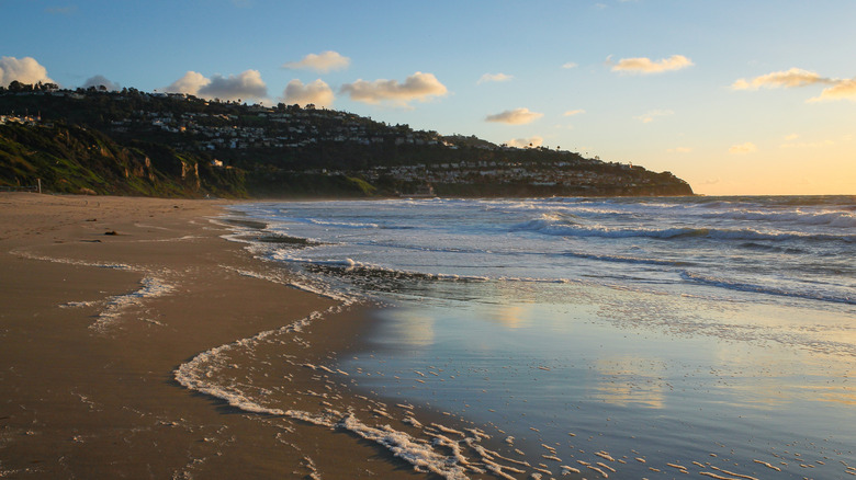 Waves washing up on a sandy beach at sunset with houses on hills in the background in Torrance, California