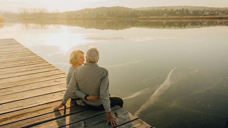 A retired couple enjoys a peaceful moment on the doc overlooking a tranquil lake.