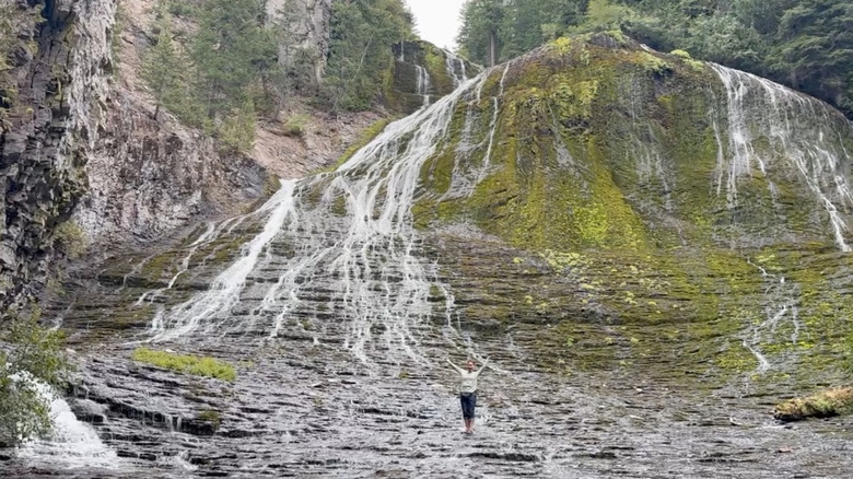Hiker posing with cascading waterfall over mossy rocks
