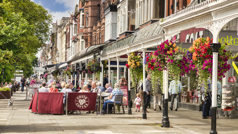 View of Lord Street in Southport, UK in spring, with baskets of flowers hanging from eaves and people sitting at an outdoor cafe