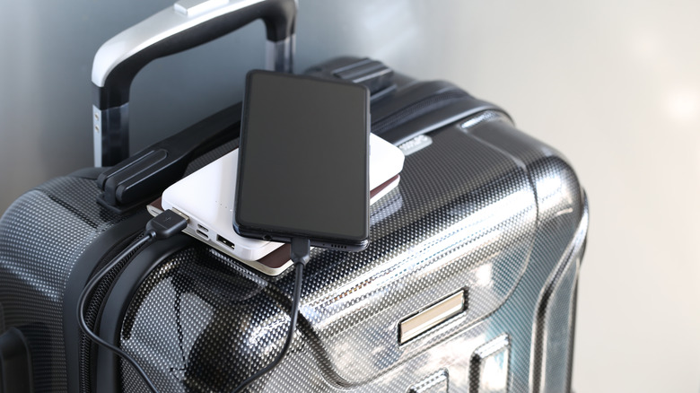 Black phone plugged into a white power bank on top of gray hard-sided luggage