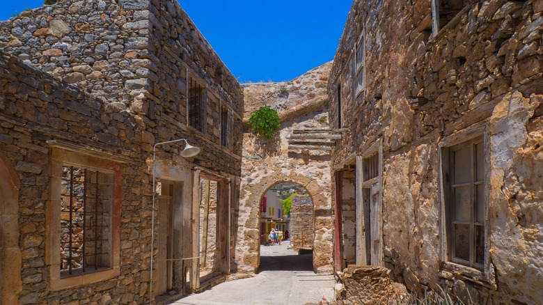 A thin street on Spinalonga with abandoned brick buildings and a small archway
