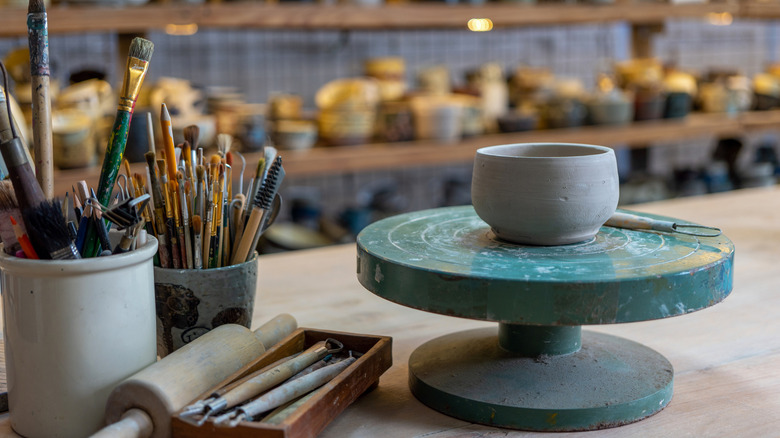 Pottery bowl on wheel, paintbrushes, pots on shelves
