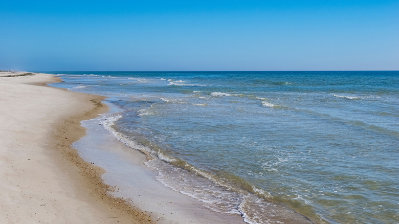 Calm blue waves lap a deserted white sand beach on St. George Island, Florida.