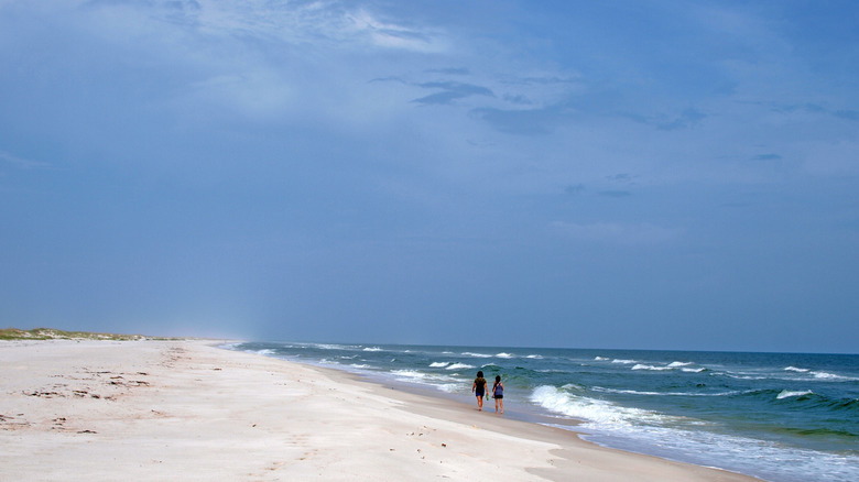 Two people walk on an empty white sand beach at St. George Island State Park, in Florida.