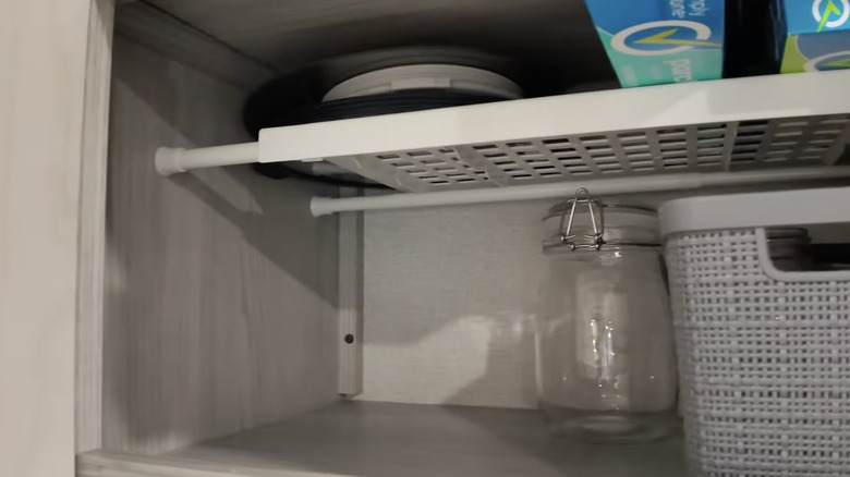 A small metal shelf sits on a couple of short tension rods inside of a cabinet