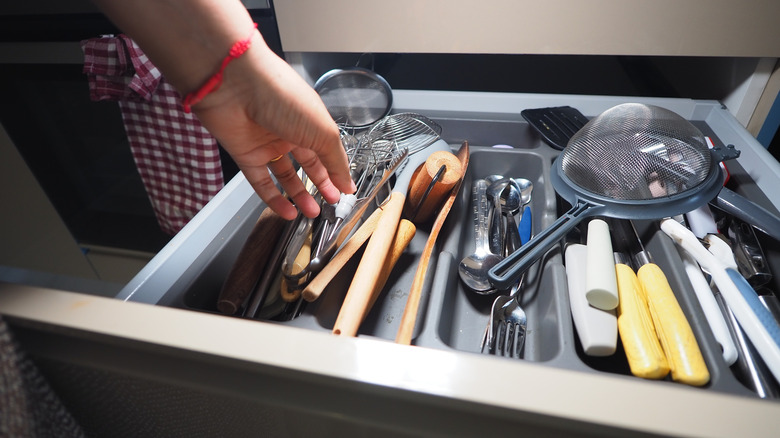 Organizing kitchen utensils in a tray in a cluttered drawer