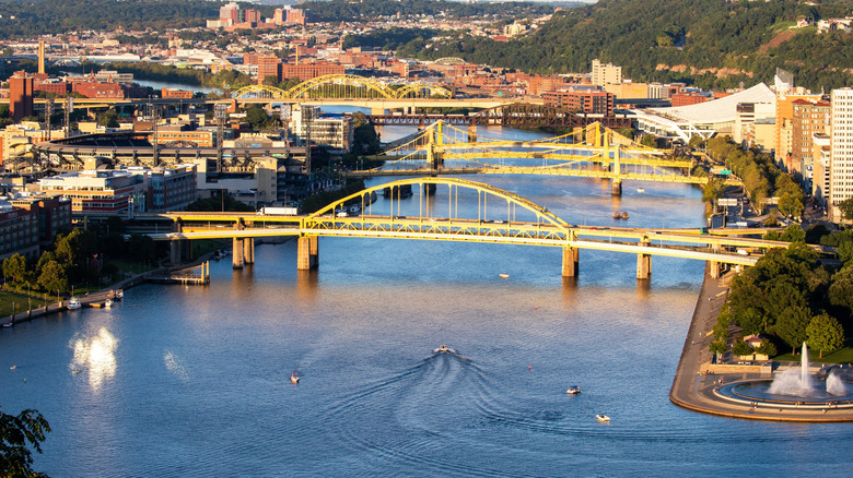 PIttsburgh's Allegheny River crossed by yellow bridges, with a fountain in the foreground and cityscape in the background