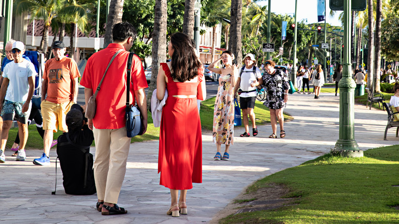 People in Hawai'i walking on large pedestrian path next to a street surrounded by palm trees