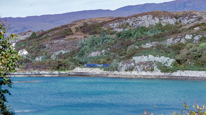 Train on the Kyle Line in Scotland traveling past blue water alongside rugged mountains