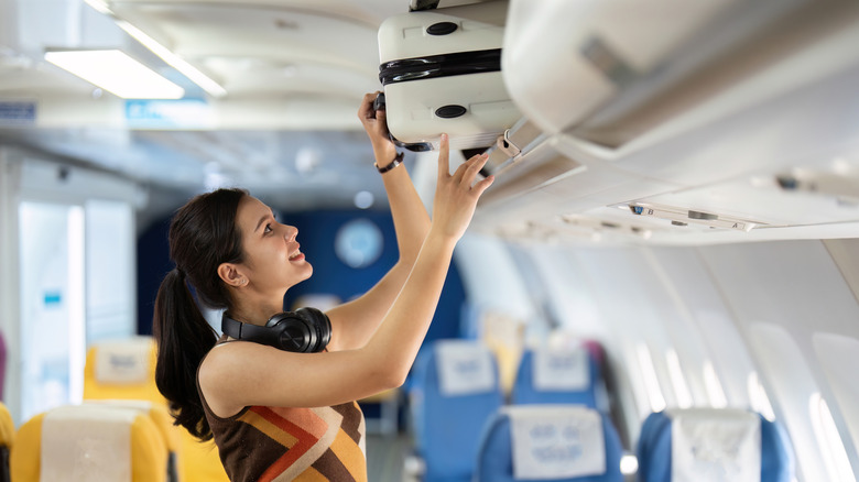 a woman loading a luggage into an overhead bin