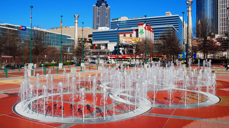 Olympic rings with water jets called the Fountain of Rings in Centennial Olympic Park surrounded by tall buildings.