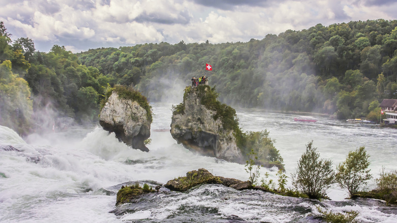 Rocky island in the middle of rushing Rhine Falls with red and white Swiss flag on top