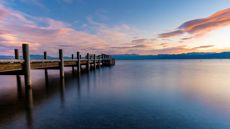 The sunset reflects across the still water beneath a wooden pier on Lake Tahoe.