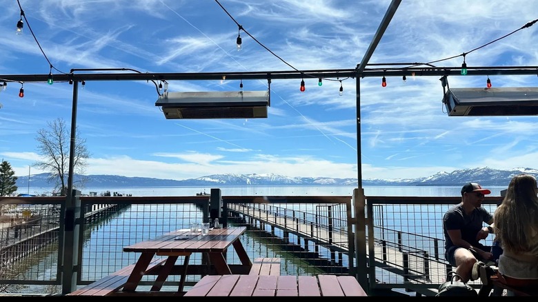 Heat lamps and string lights hang over a restaurant's lakefront patio overlooking Lake Tahoe.